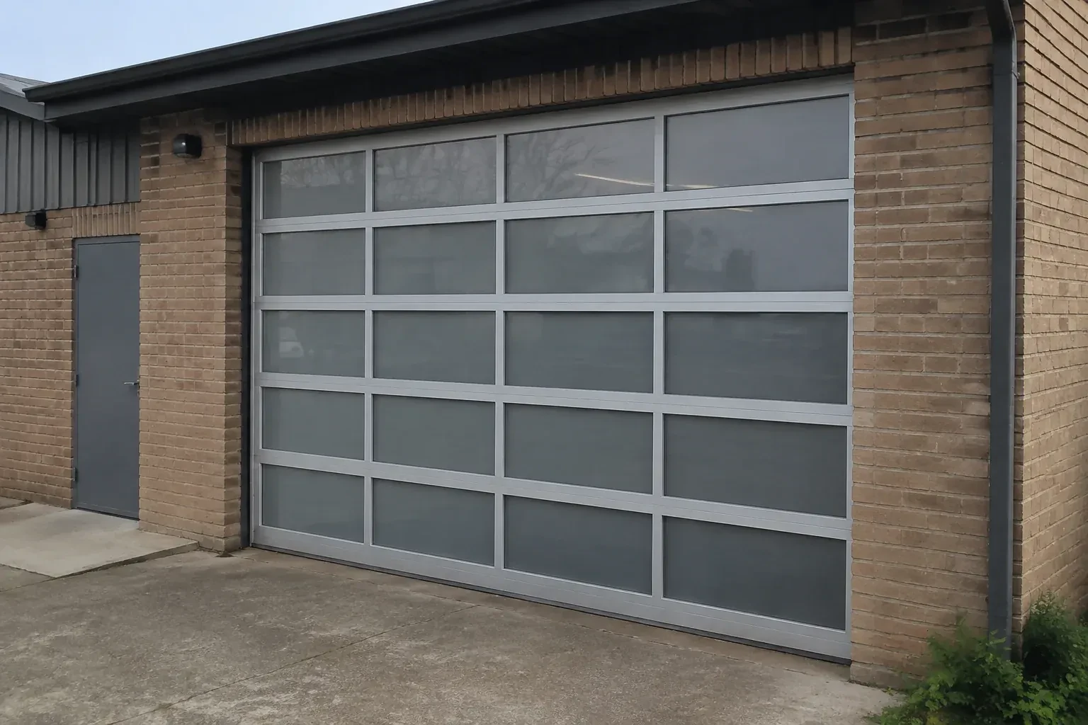 Closed glazed sectional door in a grey metal frame at a brick workshop. — Full-View Glass Garage Door Installation, Peterborough