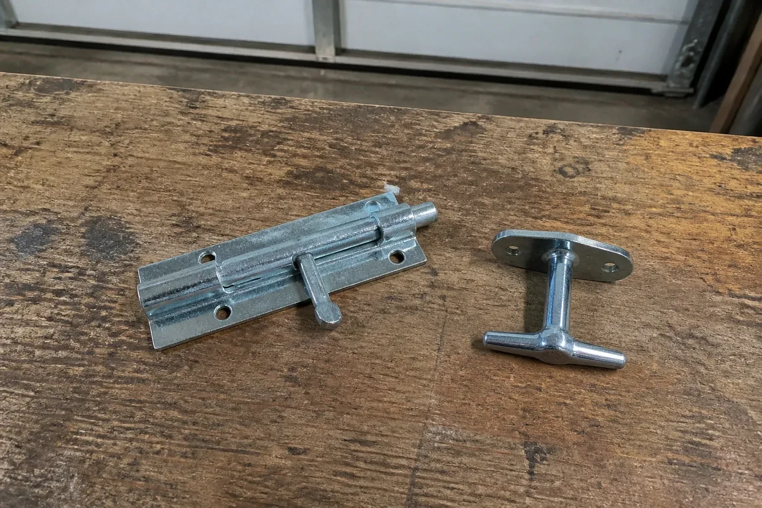 Detached slide bolt and T-handle on a wooden garage workbench. — Garage Door Manual Lock Repair, Westmount