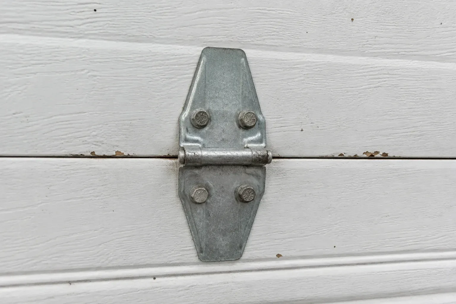Metal center hinge across a seam in a white sectional garage door. — Garage Door Hinge Replacement, Peterborough