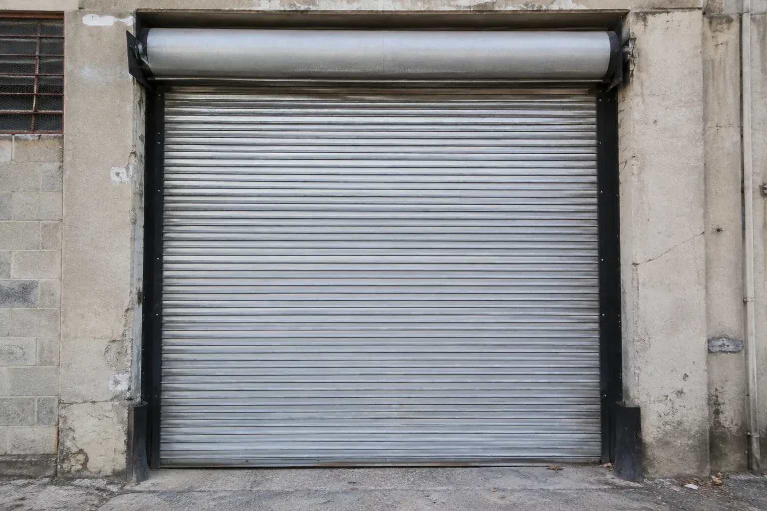 Closed metal rolling shutter in a weathered warehouse opening. — Commercial Rolling Door Repair, Peterborough