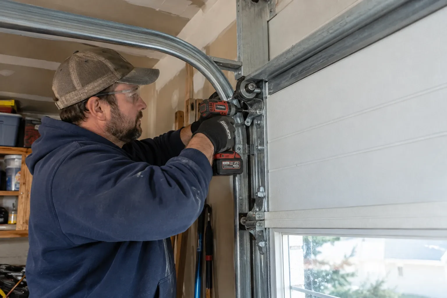 Technician in a mesh cap driving a screw with a cordless drill into a roller bracket beside a curved metal track. — Westmount