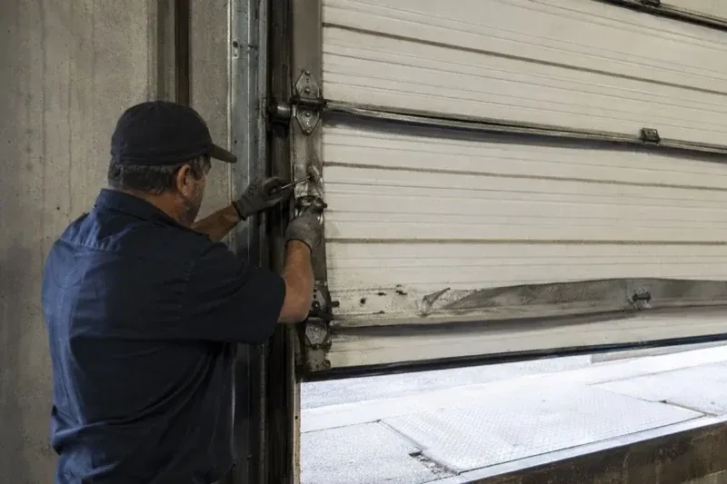 Person holding tools at the side hinge of a partly raised industrial sectional door — Commercial Sectional Door Repair, Peterborough